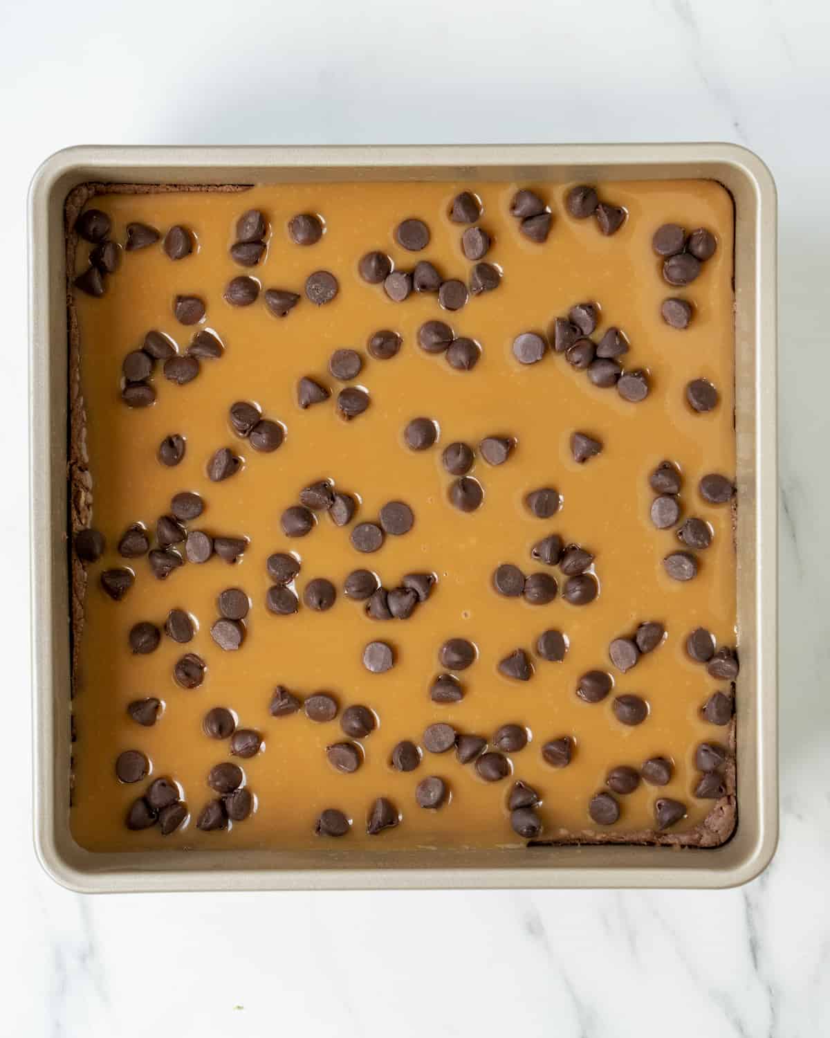Chocolate chips have been sprinkled on top of the layer of caramels in the square baking pan.  