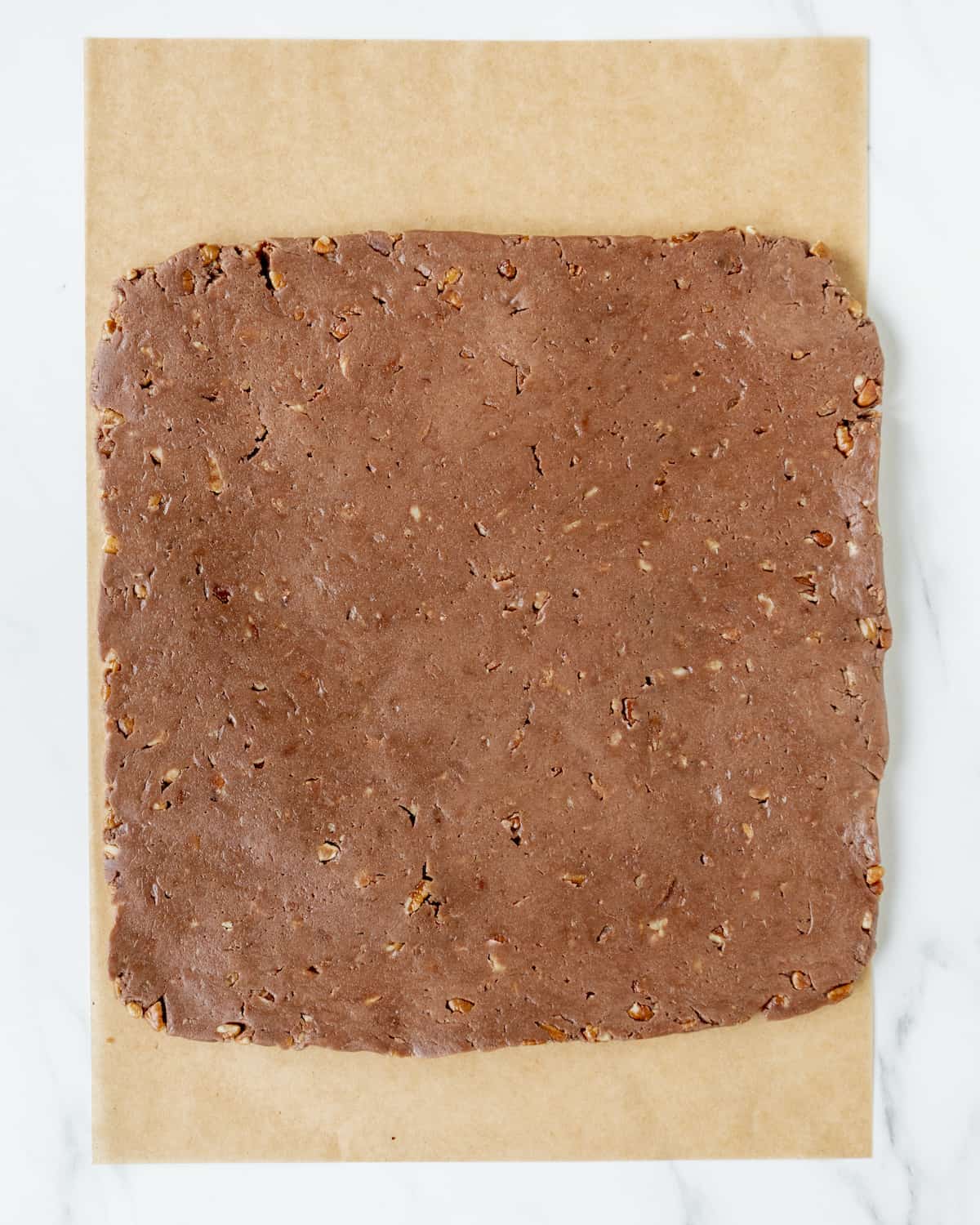 The unused brownie dough has been hand pressed into a large square on a piece of parchment paper.  