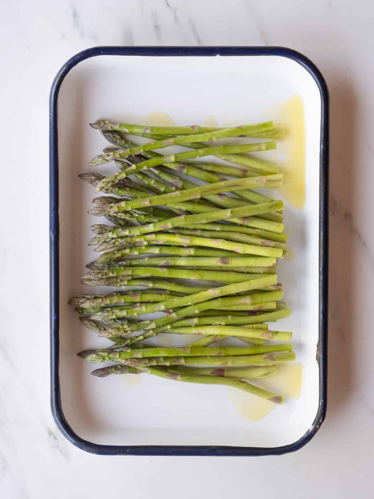 A rectangular platter with asparagus drizzled with olive oil.