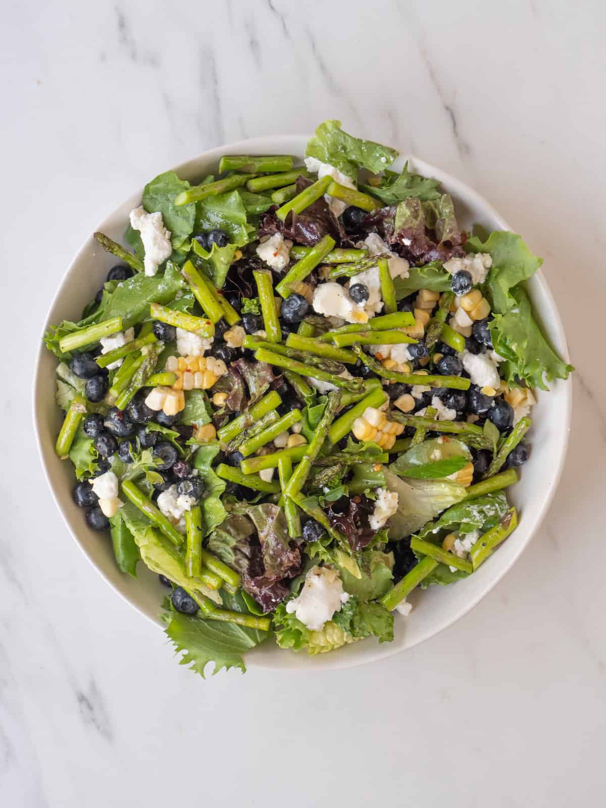 A large bowl with all the ingredients for salad tossed together, and grilled asparagus added on top along with champagne vinaigrette drizzled.