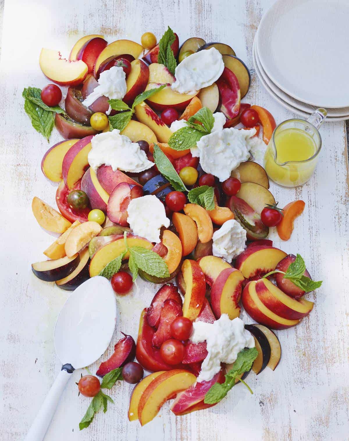 An overhead shot of a stone fruit and burrata salad, with mint and heirloom tomatoes.