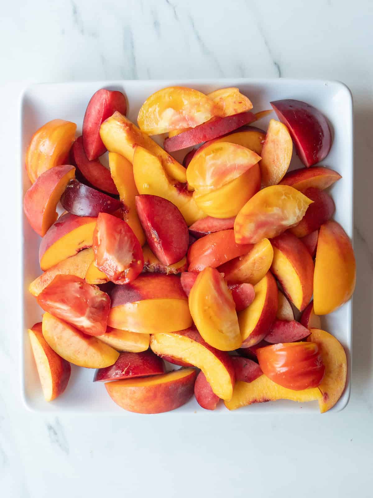 A plate with nectarines, plums, peaches and heirloom tomato wedges all mixed together.