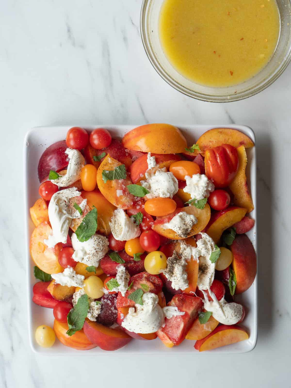 A plate with stone fruit and burrata salad with a bowl of champagne vinaigrette.