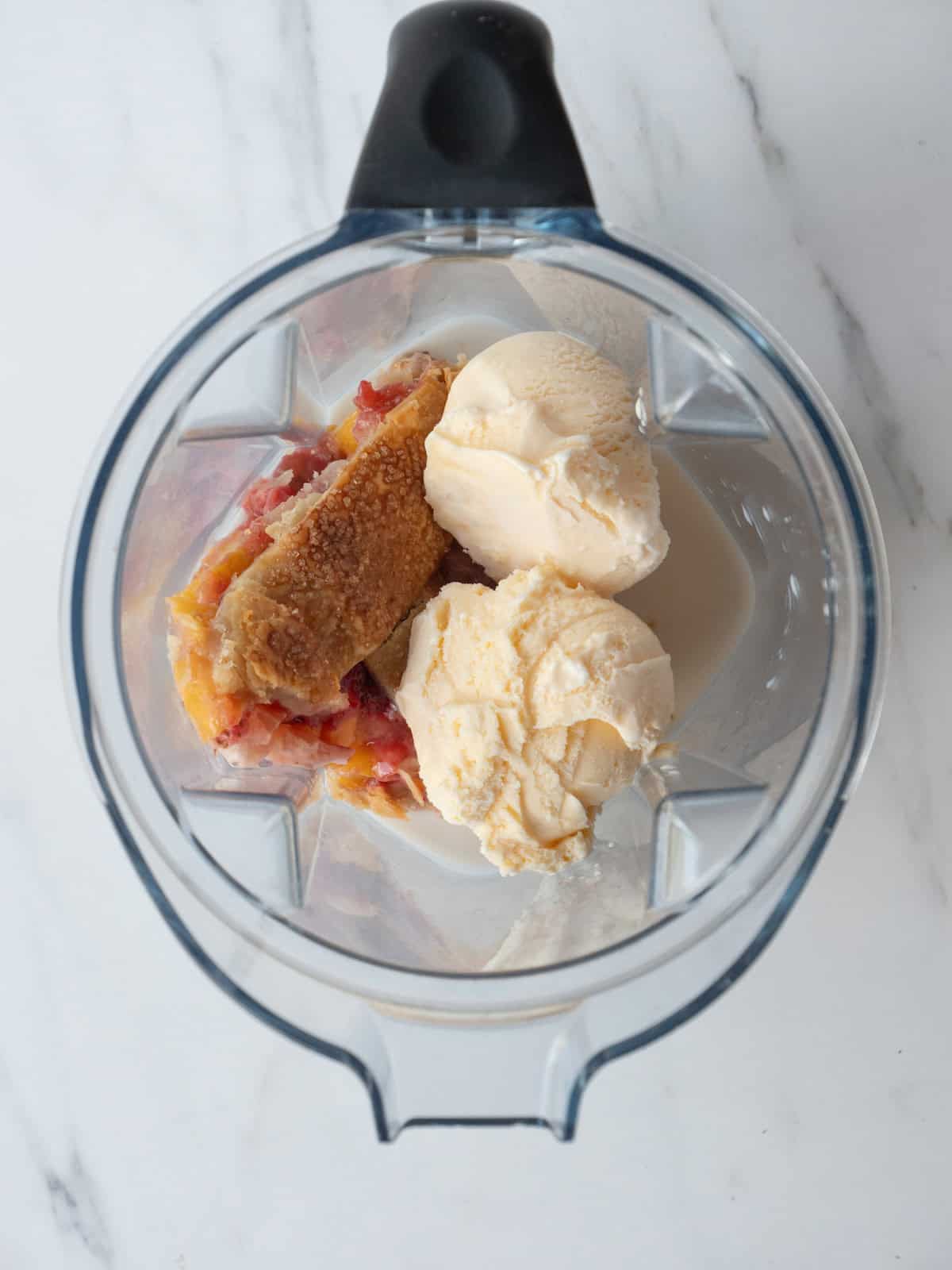 A blender jar with two scoops of vanilla ice cream, a slice of strawberry peach pie and almond milk.