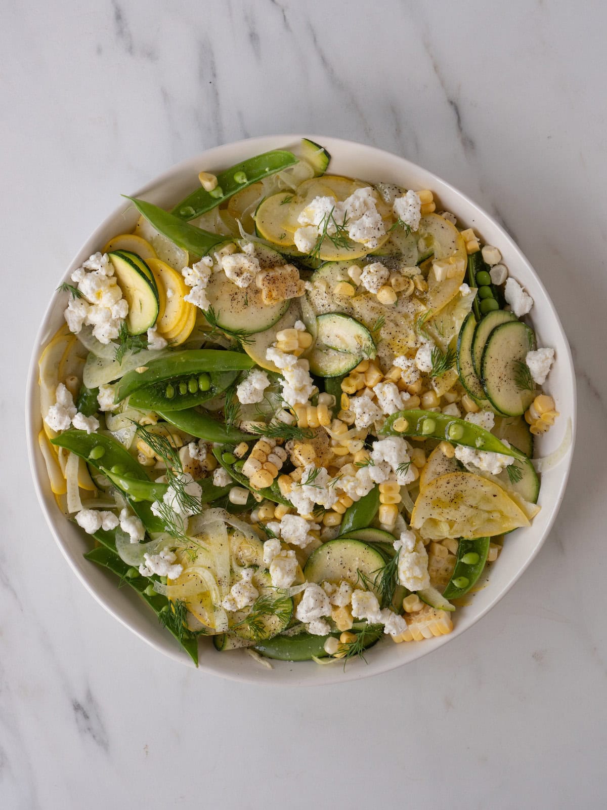 A bowl with a raw summer salad with lemon juice and olive oil added.