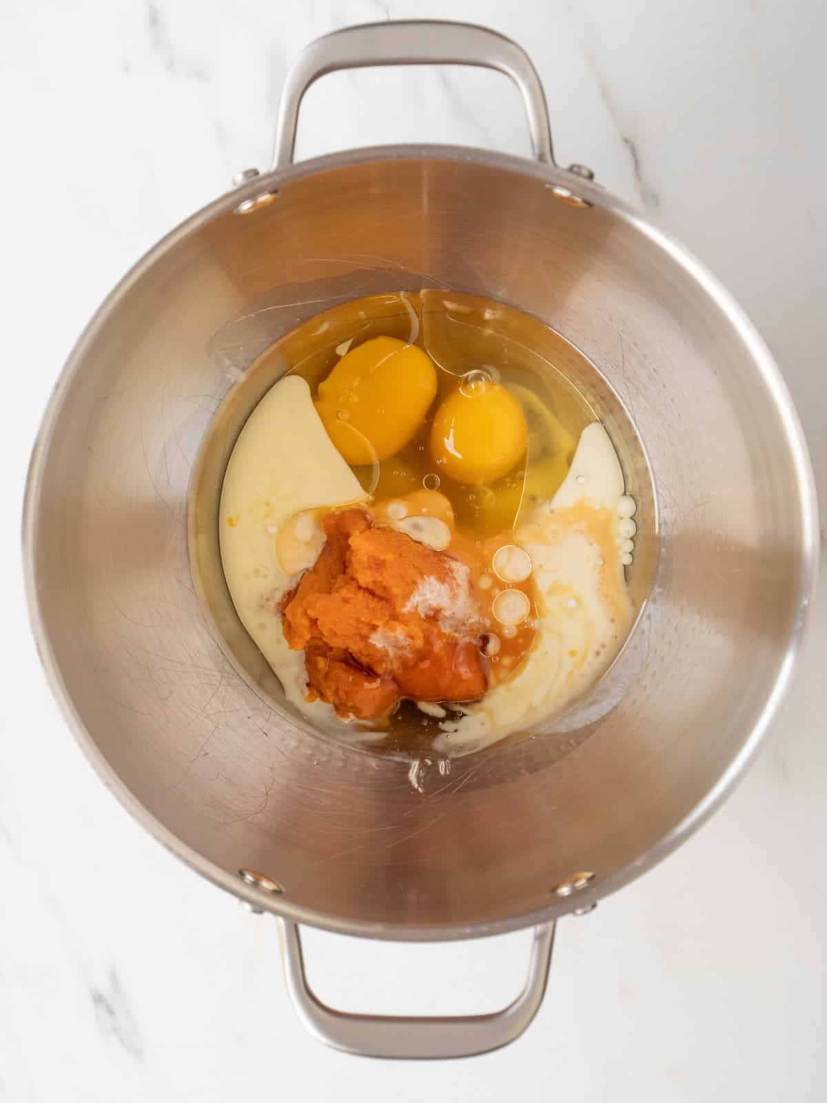A stand mixer bowl with all wet ingredients to make donut batter.