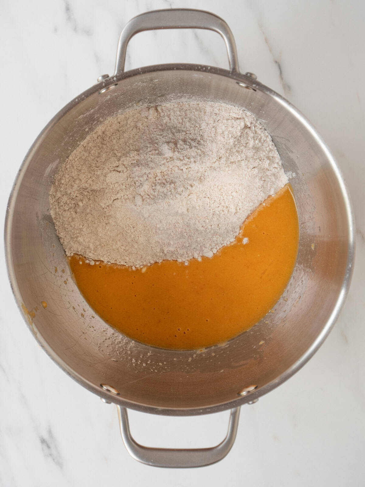 A stand mixer bowl with all wet ingredients mixed together, and mix of dry ingredients added to make donut batter.