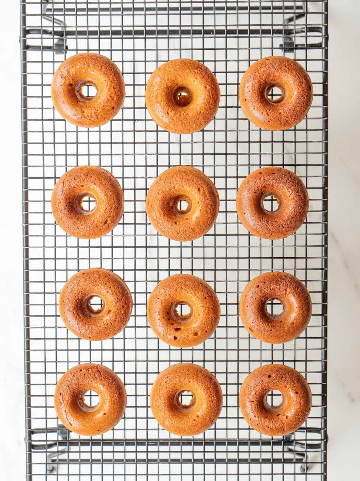 A wire rack with baked spiced pumpkin donuts fresh out of the oven.