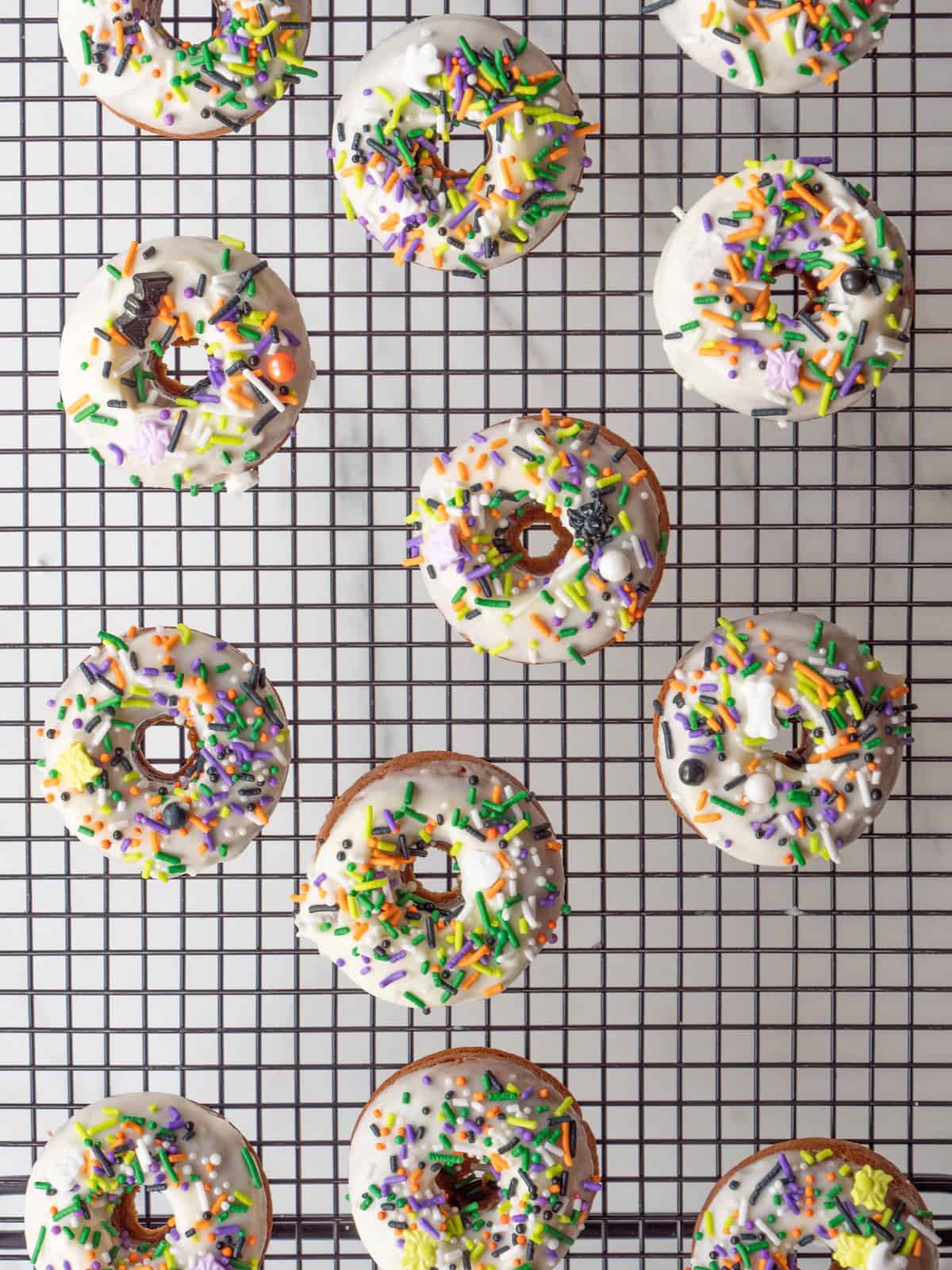 A wire rack with freshly baked spiced pumpkin donuts dipped in icing and decorated with sprinkles.