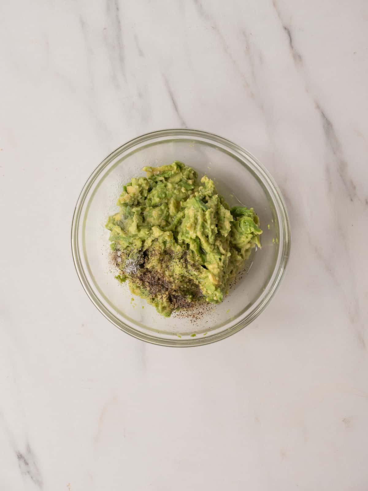 A mixing bowl with avocado, mashed with lemon juice, salt and pepper.