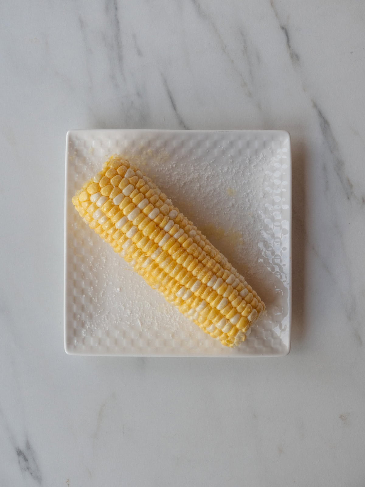 A plate with a corn on the cob on it brushed with olive oil and sprinkled with salt.