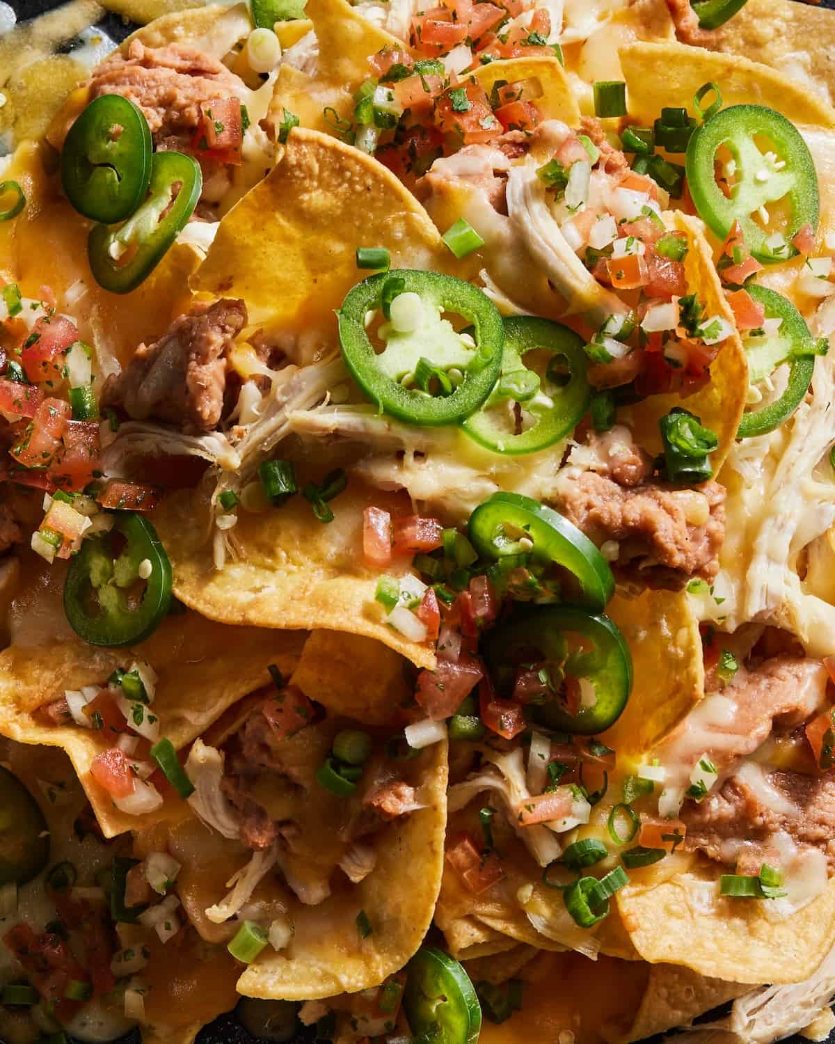 a close up of Grilled Nachos on a oven proof baking sheet with heaps of guacamole, cheese, jalapeños, beans and more! 
