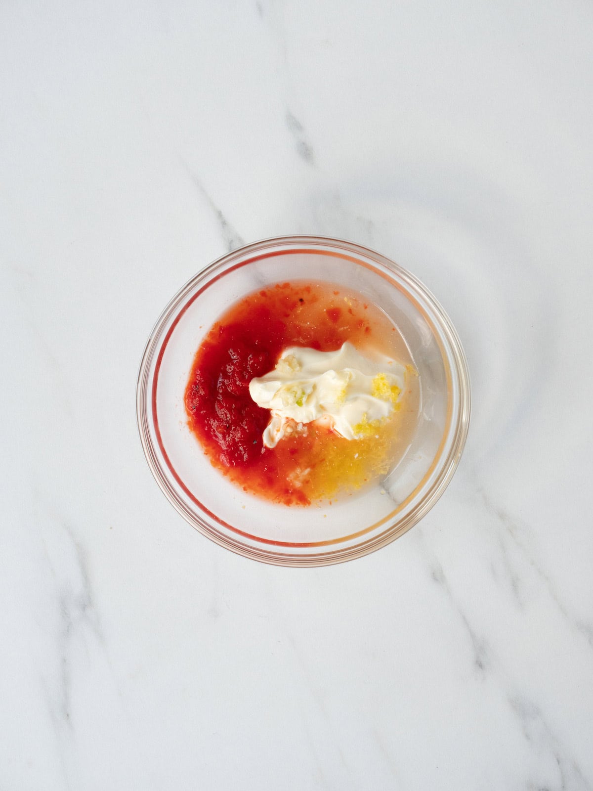 A mixing bowl with mayo, garlic, harissa paste, and lemon zest and juice.