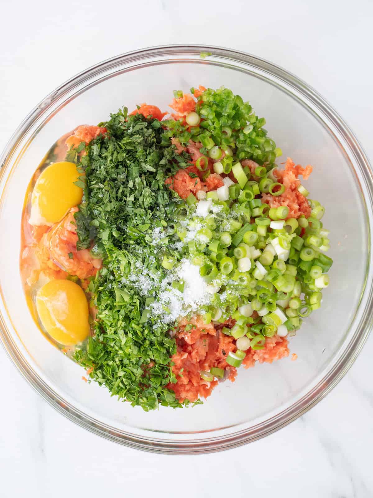 A mixing bowl with finely diced salmon, green onions, cilantro, parsley, jalapeño, eggs, olive oil and salt.