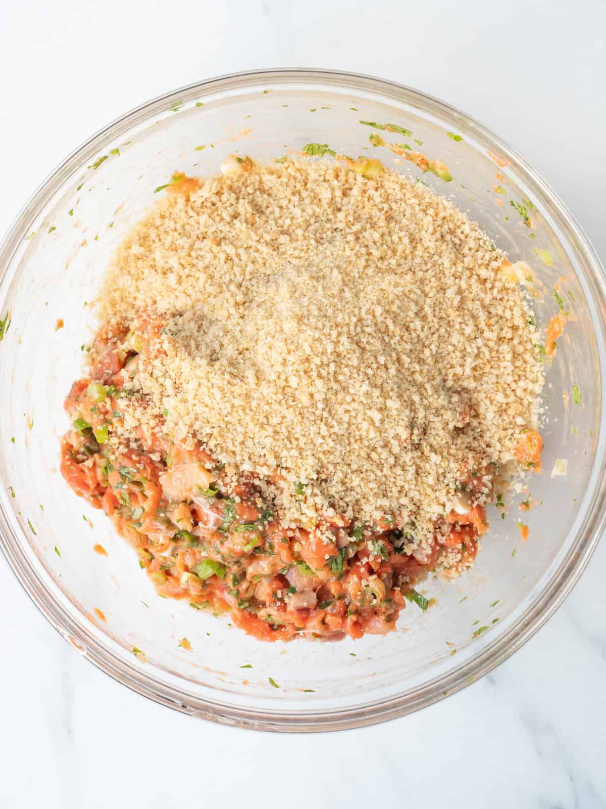 A mixing bowl with a salmon burger mixture with panko bread crumbs added.