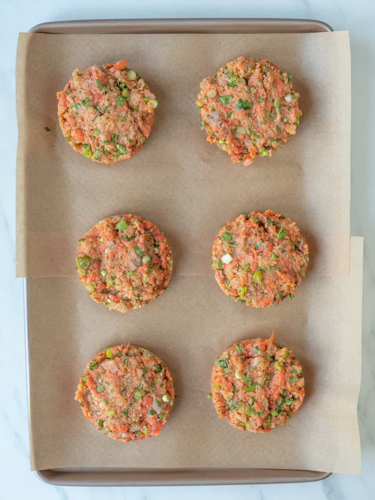 A parchment paper lined baking sheet with spiced salmon patties ready to go on the grill.