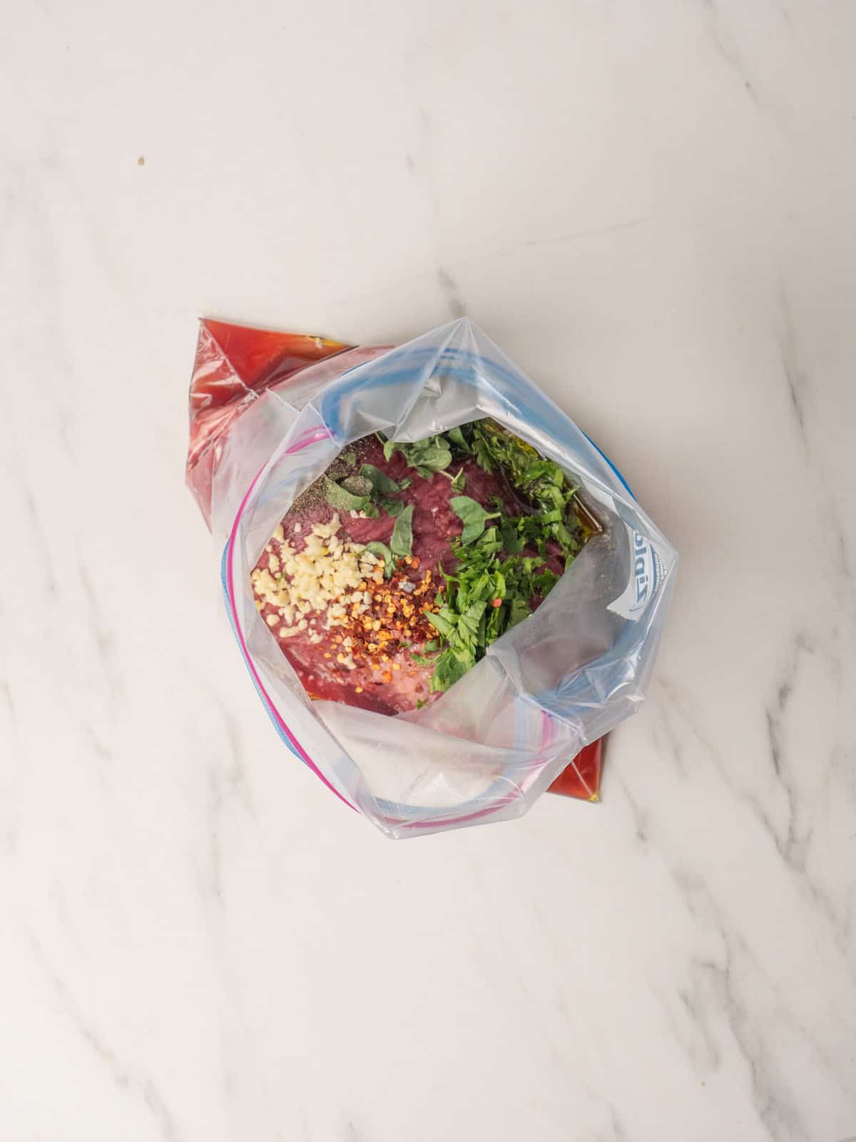 A zip top bag with ingredients for marinade and the flank steak added to it.