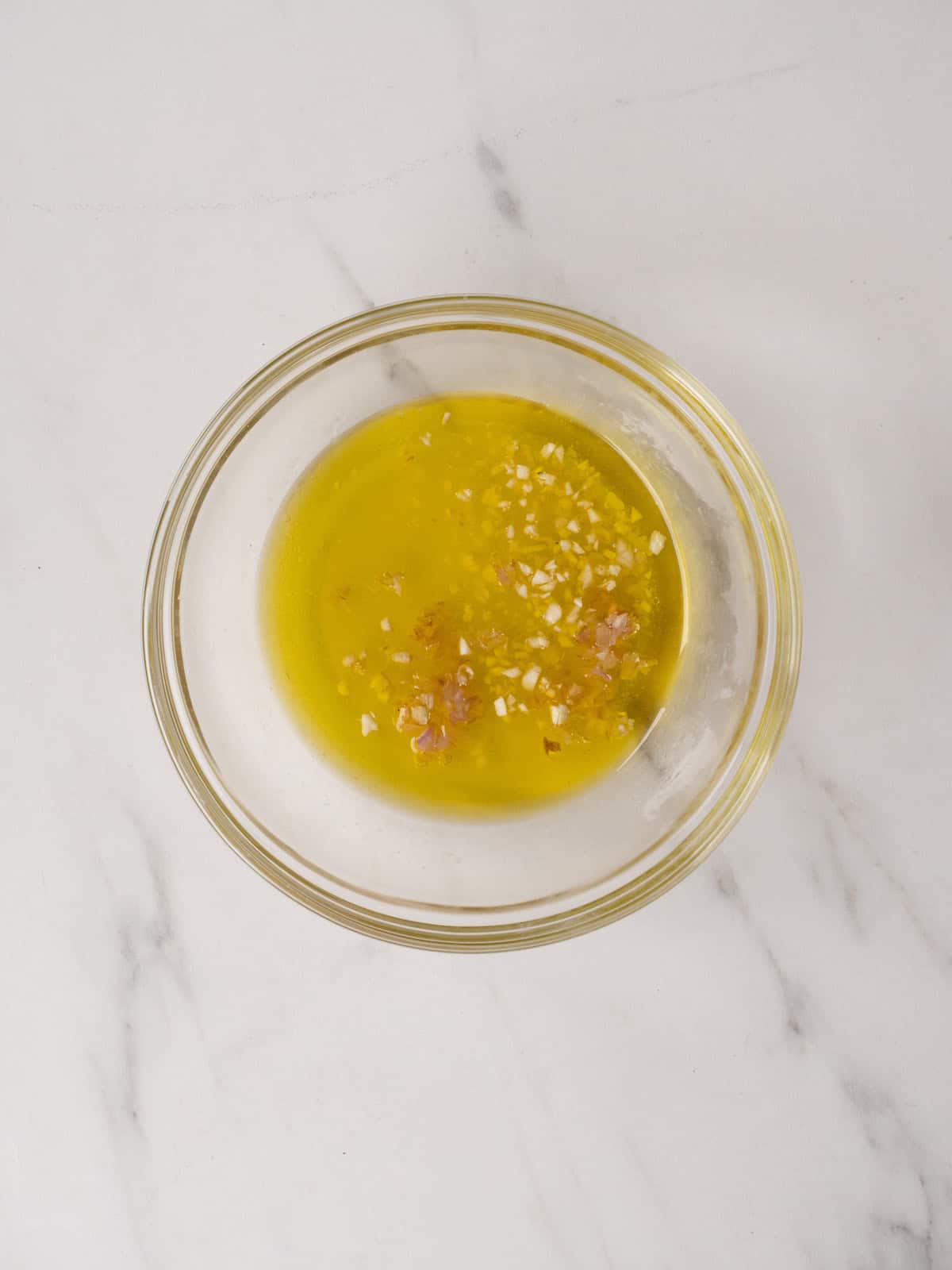 A glass mixing bowl with olive oil, lemon juice, shallot, garlic, salt and pepper to create a dressing for the lettuce leaves.