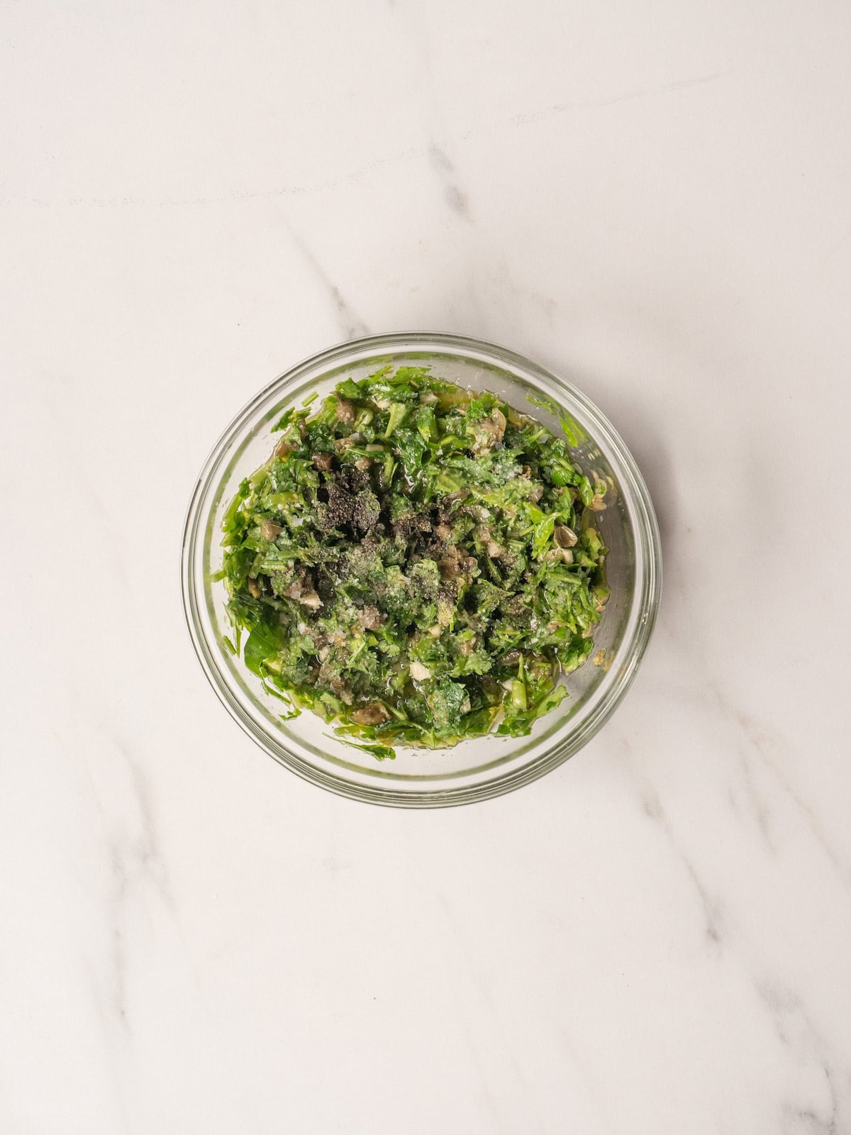 A glass mixing bowl with salsa verde.