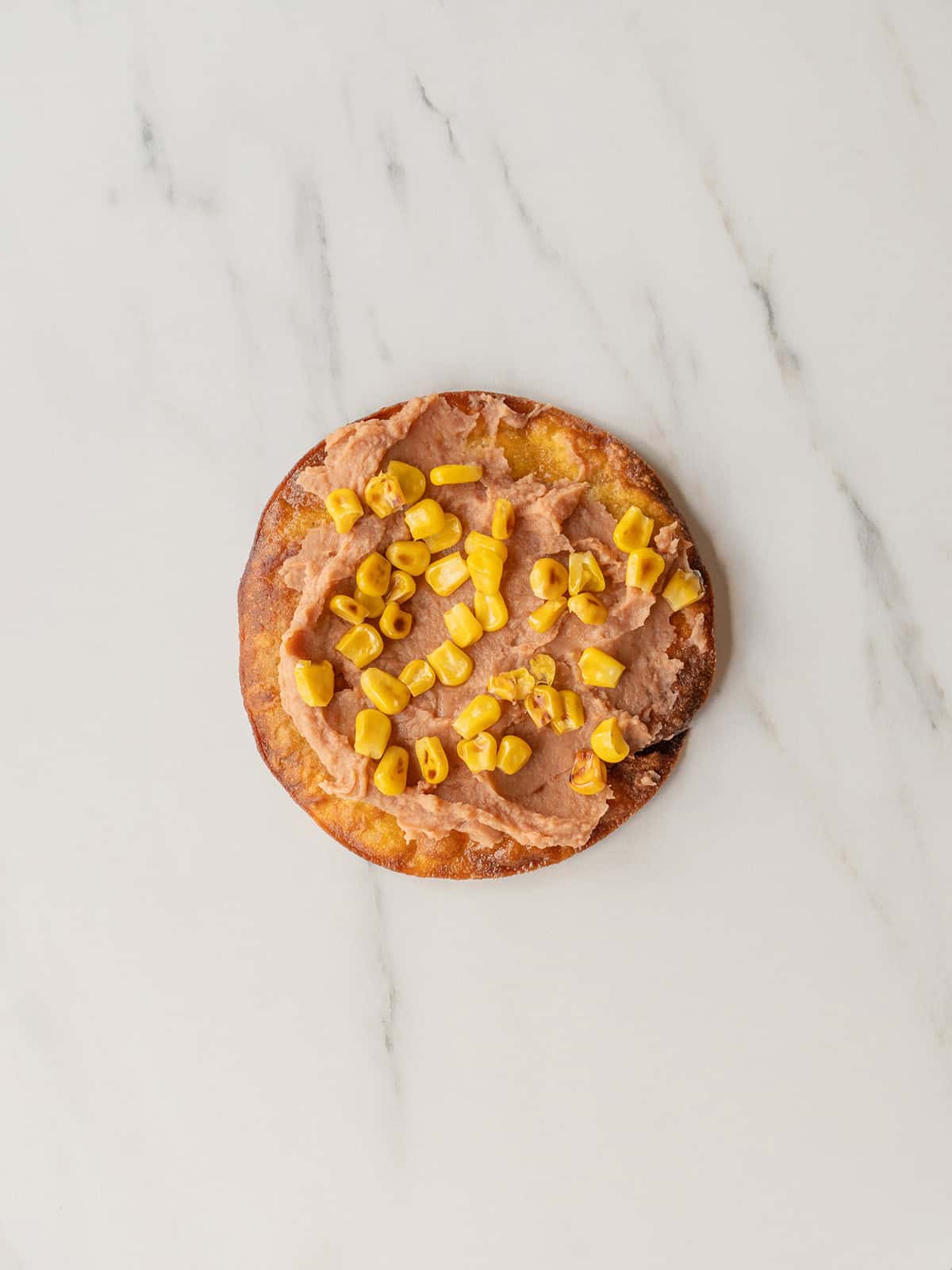 Tostada topped with refried beans and corn