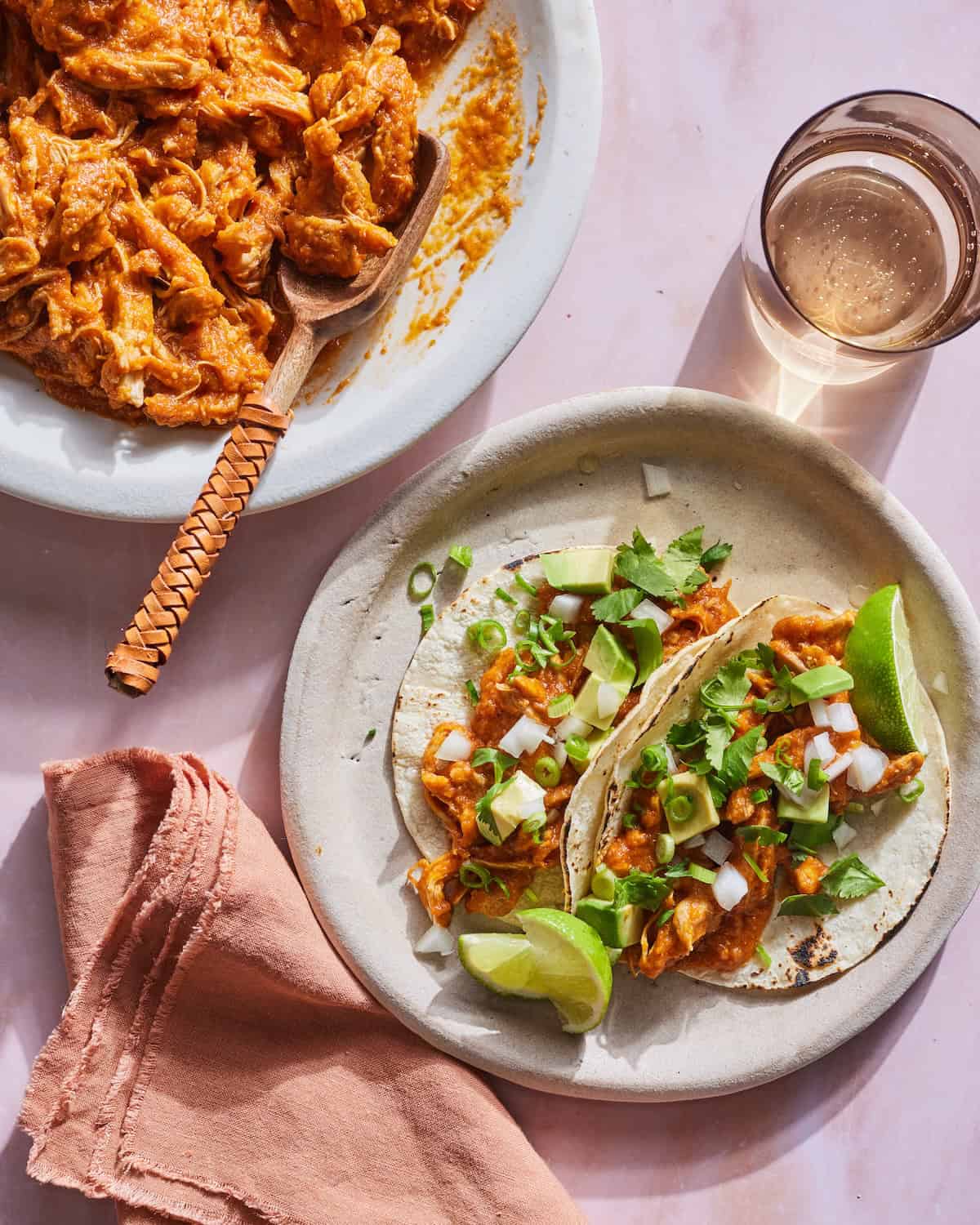 Two Chicken Tinga Tacos in a plate with a bowl of prepped Chicken Tinga.