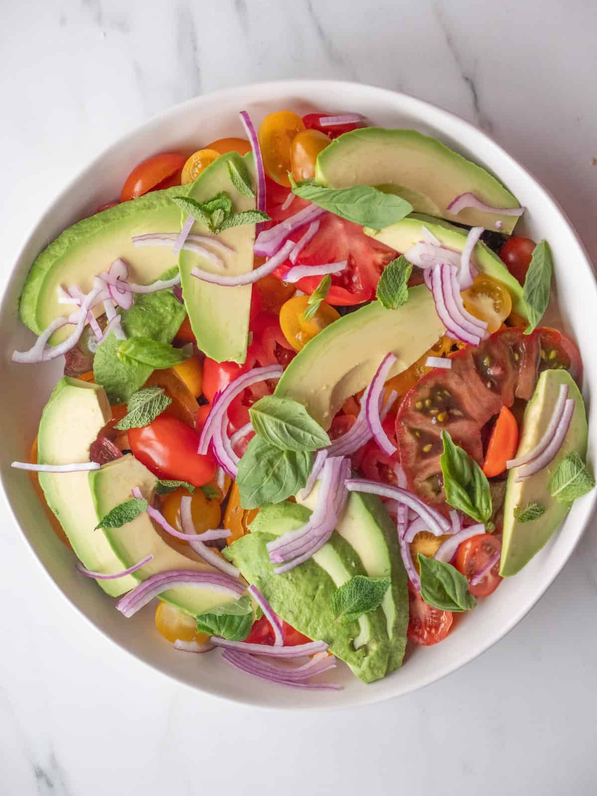 A low bowl with avocado and heirloom cherry tomato salad with onions, mint and basil.