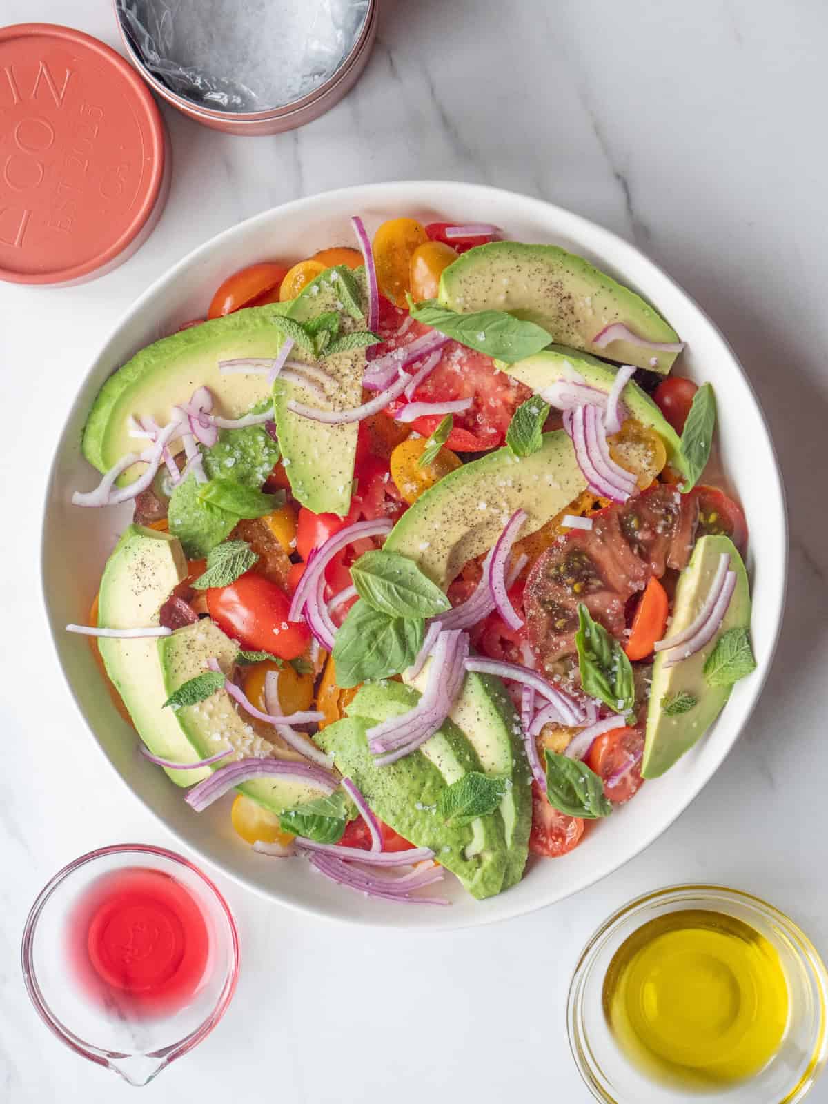 A low bowl with heirloom tomato salad with flaky salt added, along with two small bowls with red wine vinegar and olive oil.