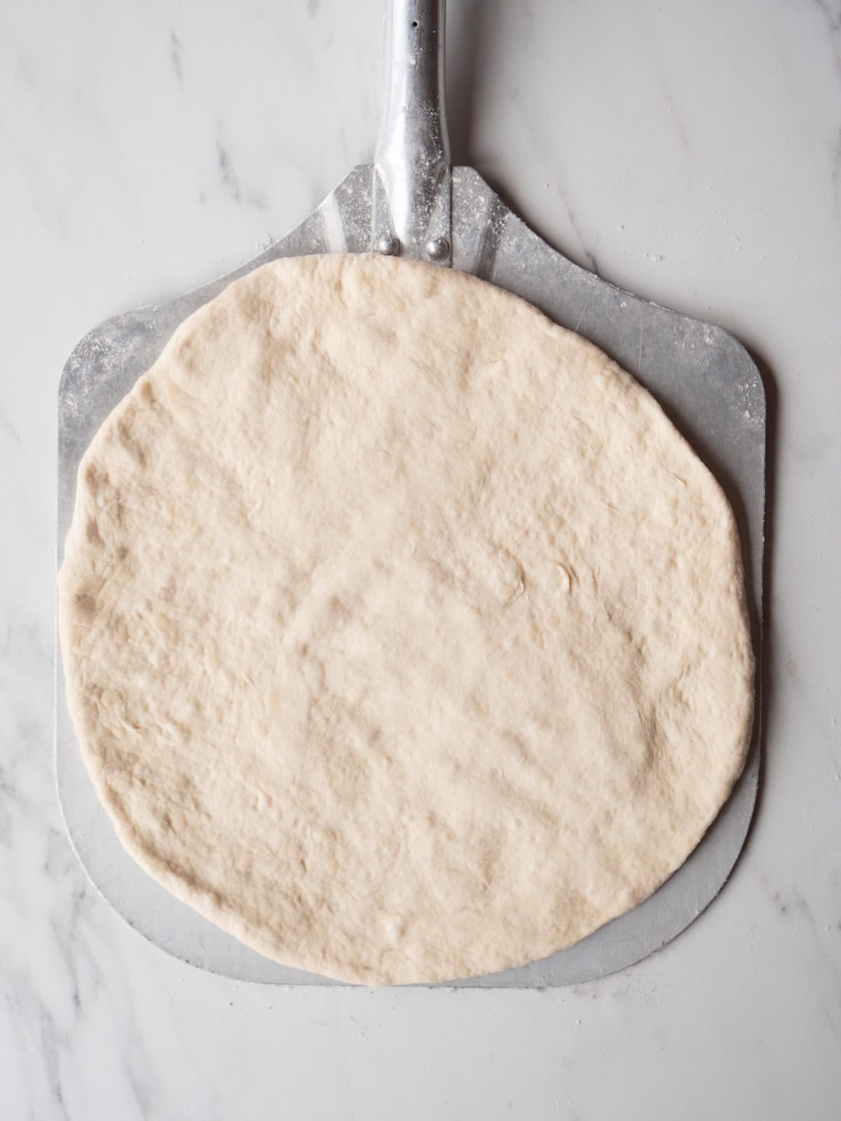 A pizza peel with a stretched out pizza dough.