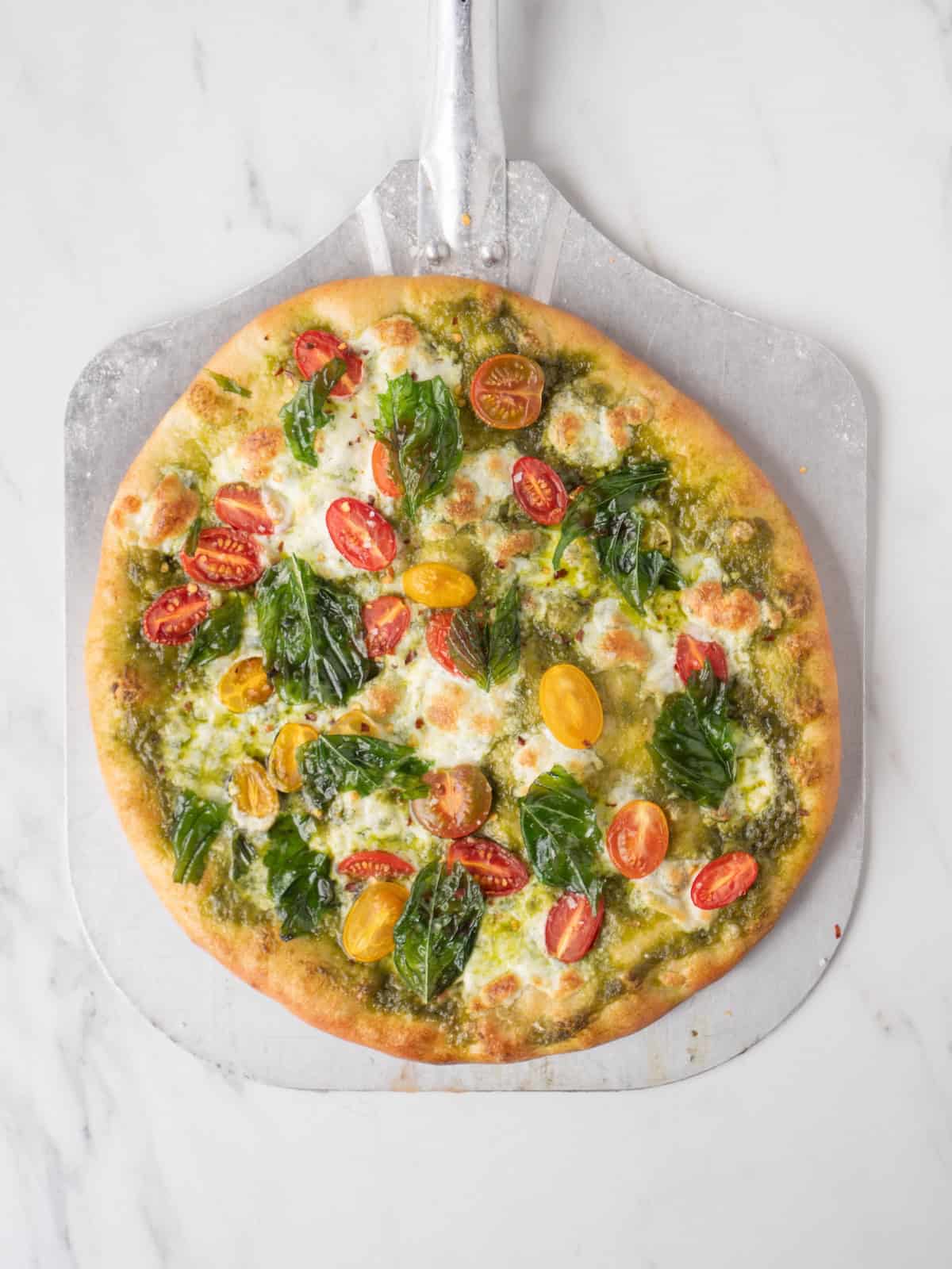 A pizza peel with a freshly baked pesto caprese pizza on it.