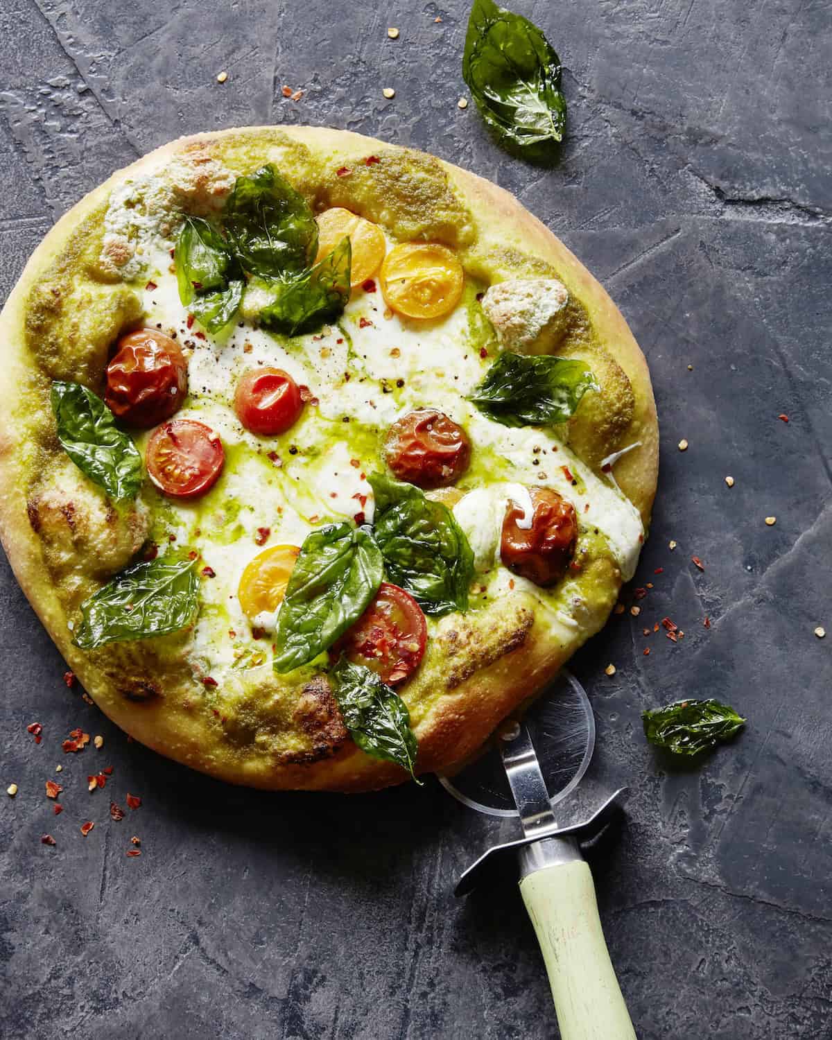 A pesto caprese pizza with a pizza cutter.