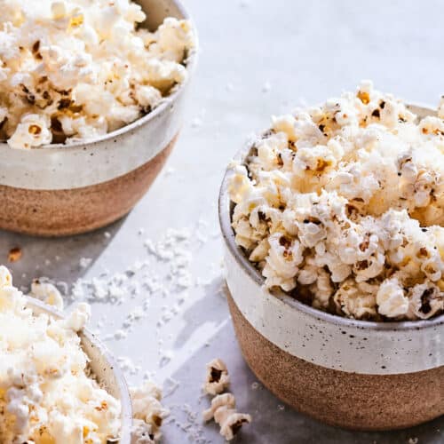 Three speckled ceramic bowls of lemon pepper popcorn on a concrete table.