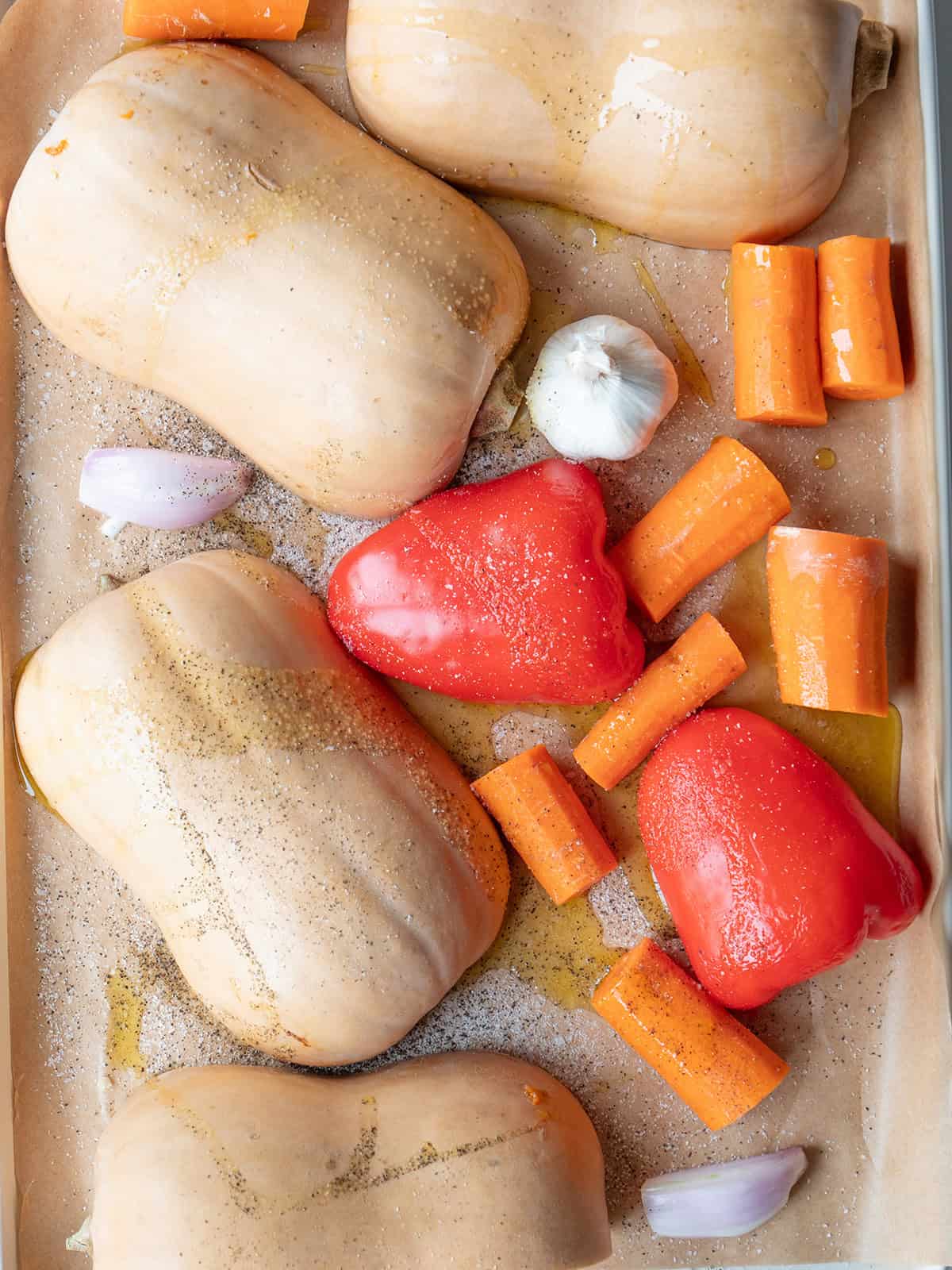 Butternut squash, carrots, bell pepper, garlic, and shallots on a baking sheet before roasting