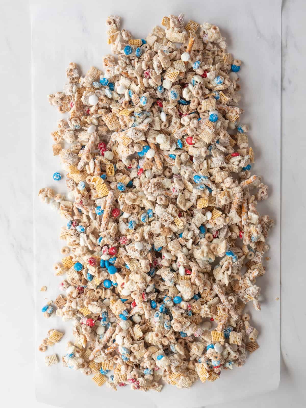 A parchment paper with a mix of cheerios, pretzels, M&Ms and chex mixed in white chocolate spread on it for it to dry.