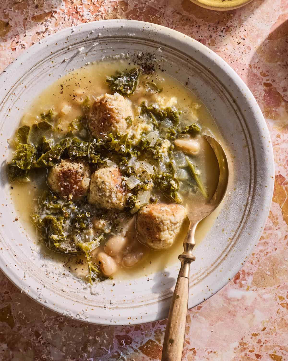 Closeup shot of a bowl of Italian Wedding Soup on a pink table.  