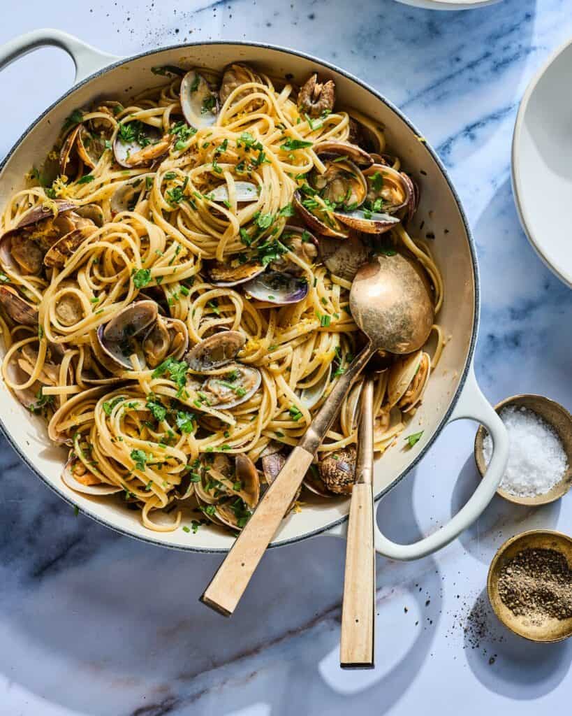 Linguini with Clams in a large braiser with serving spoons and plates