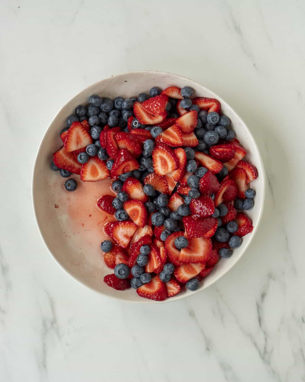 A bowl full of sugar marinated strawberries and blueberries 