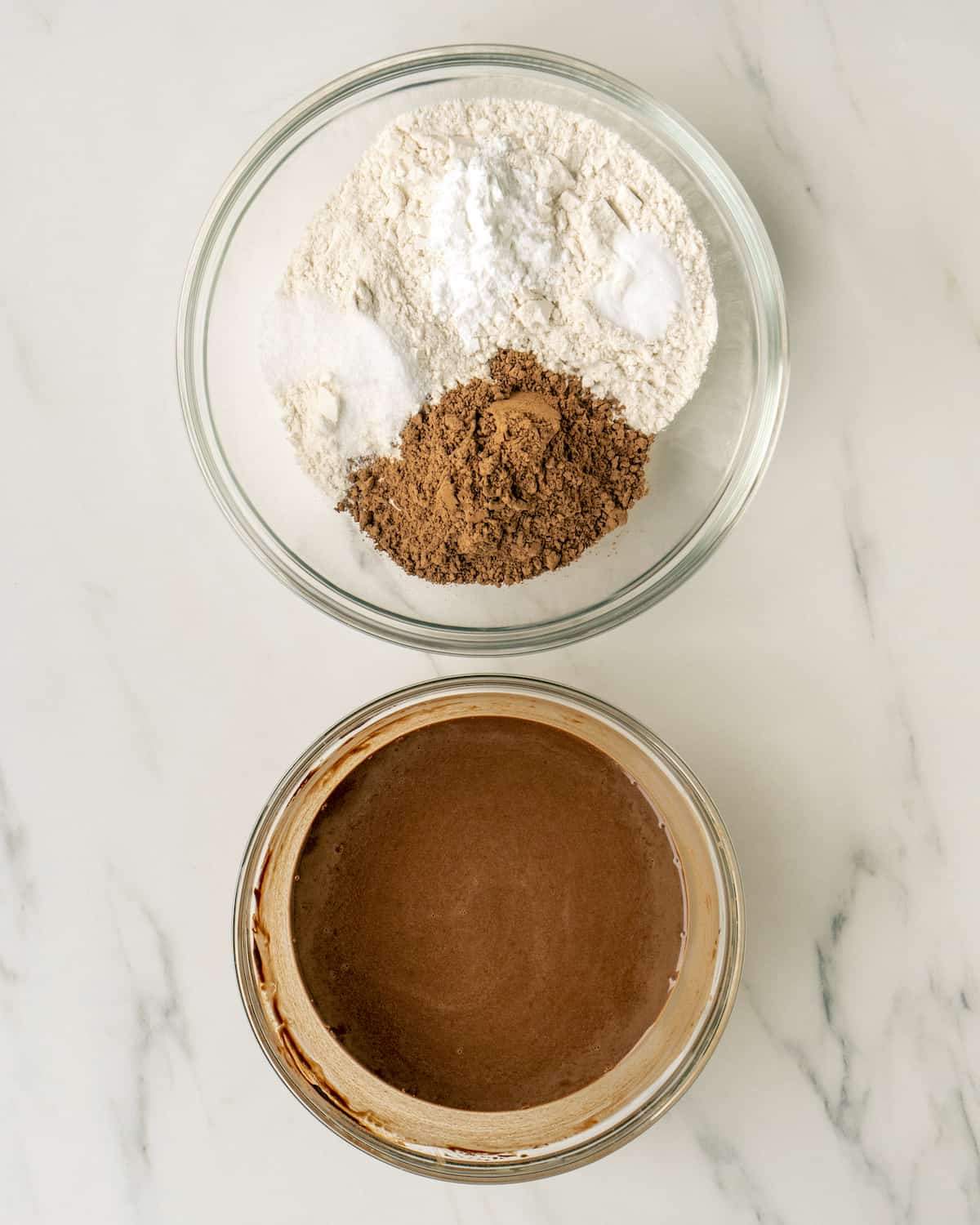 Two glass mixing bowls, one with dry ingredients: flour, cocoa powder, baking powder, baking soda and salt; and one with remaining cocoa powder and water whisked together.