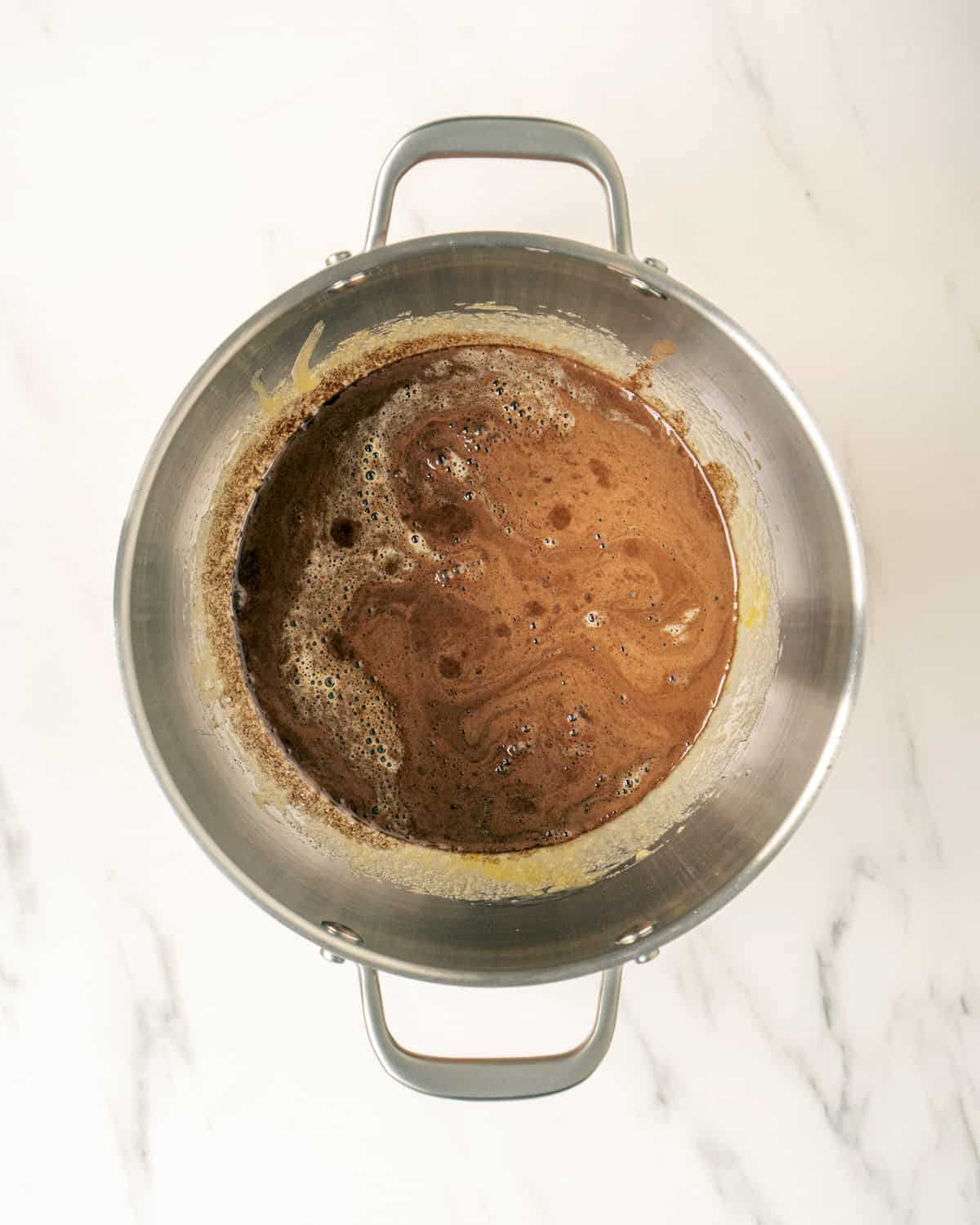 A stand mixer bowl with a batter made out of sugar, oil, eggs and the cocoa powder and water mixture. 