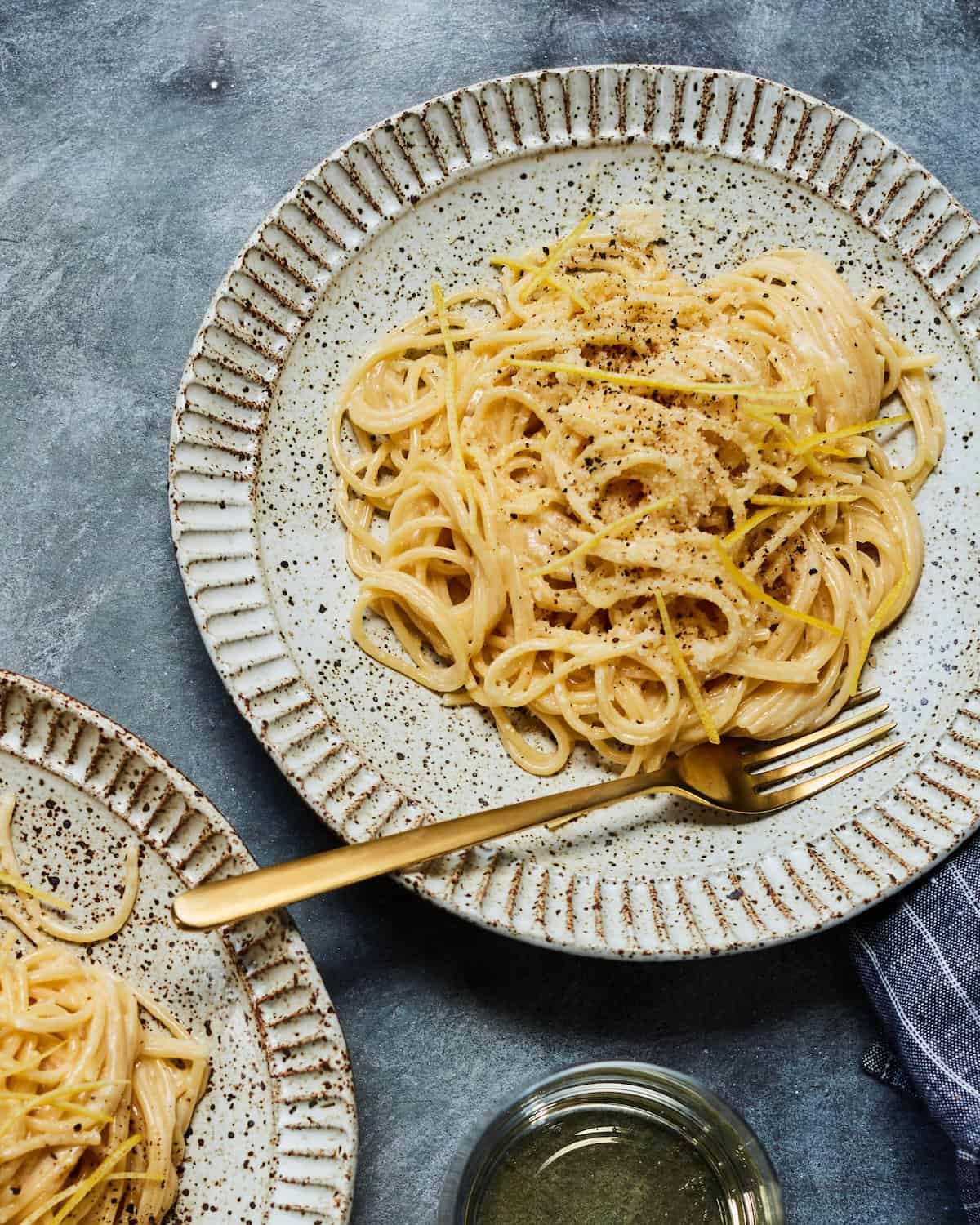 A speckled plate with a gold fork holds the final dish of Creamy Lemon Cacio e Pepe.  