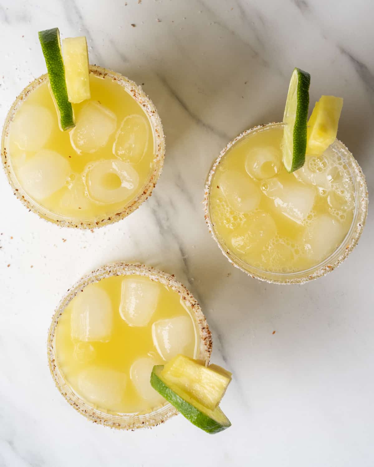 Pineapple juice, orange juice, lime juice, tequila, and ice in three tajin rimmed glasses with a lime slice and pineapple wedge garnish 