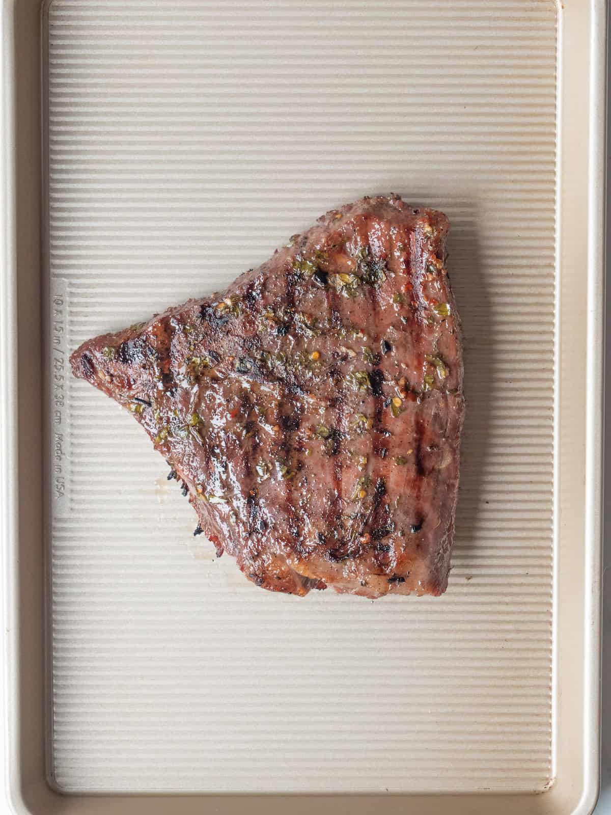 A baking sheet with flank steak that has been marinated and grilled with criss cross marks.