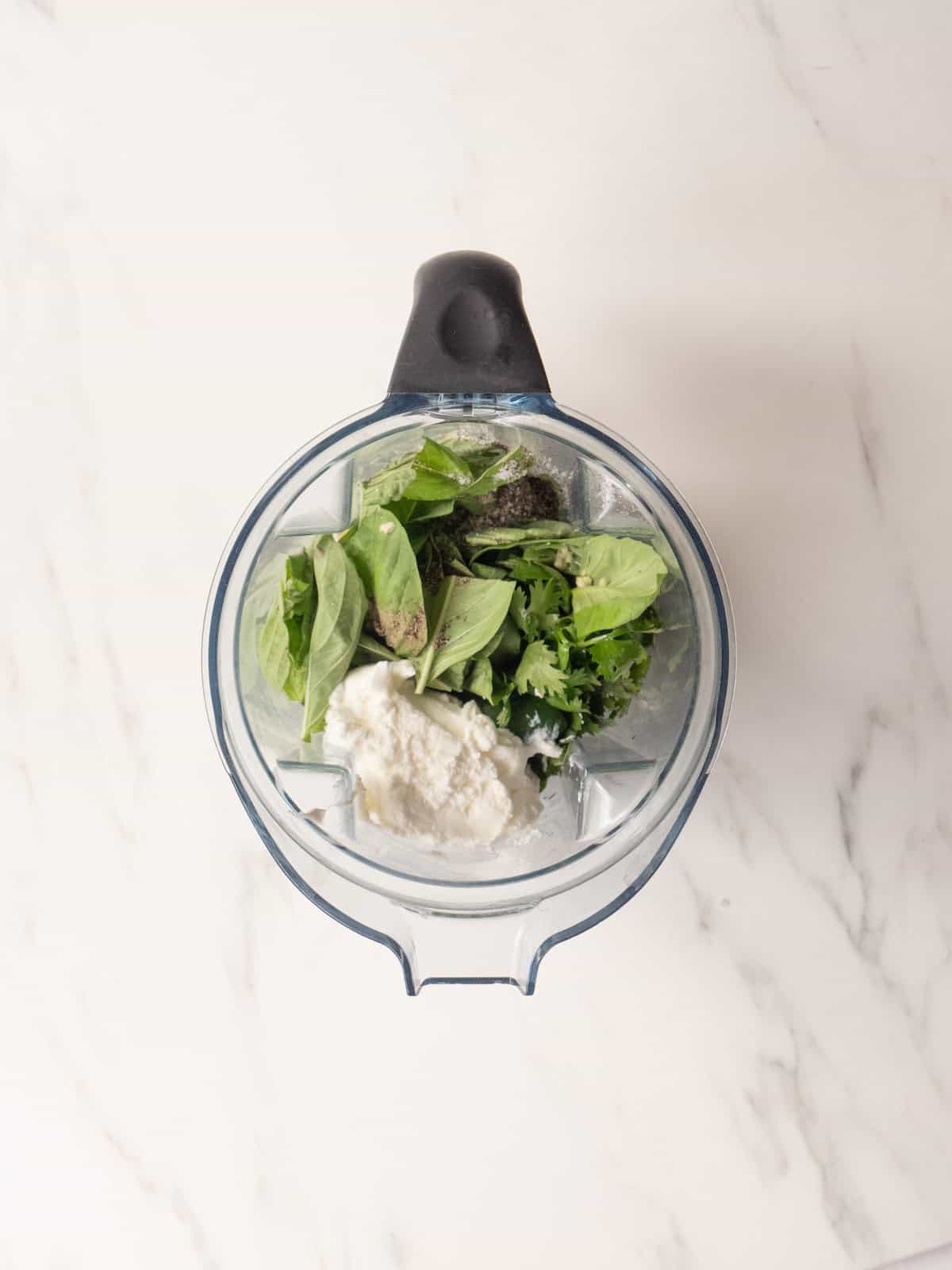 A blender jar with all ingredients to make yogurt green goddess dressing.