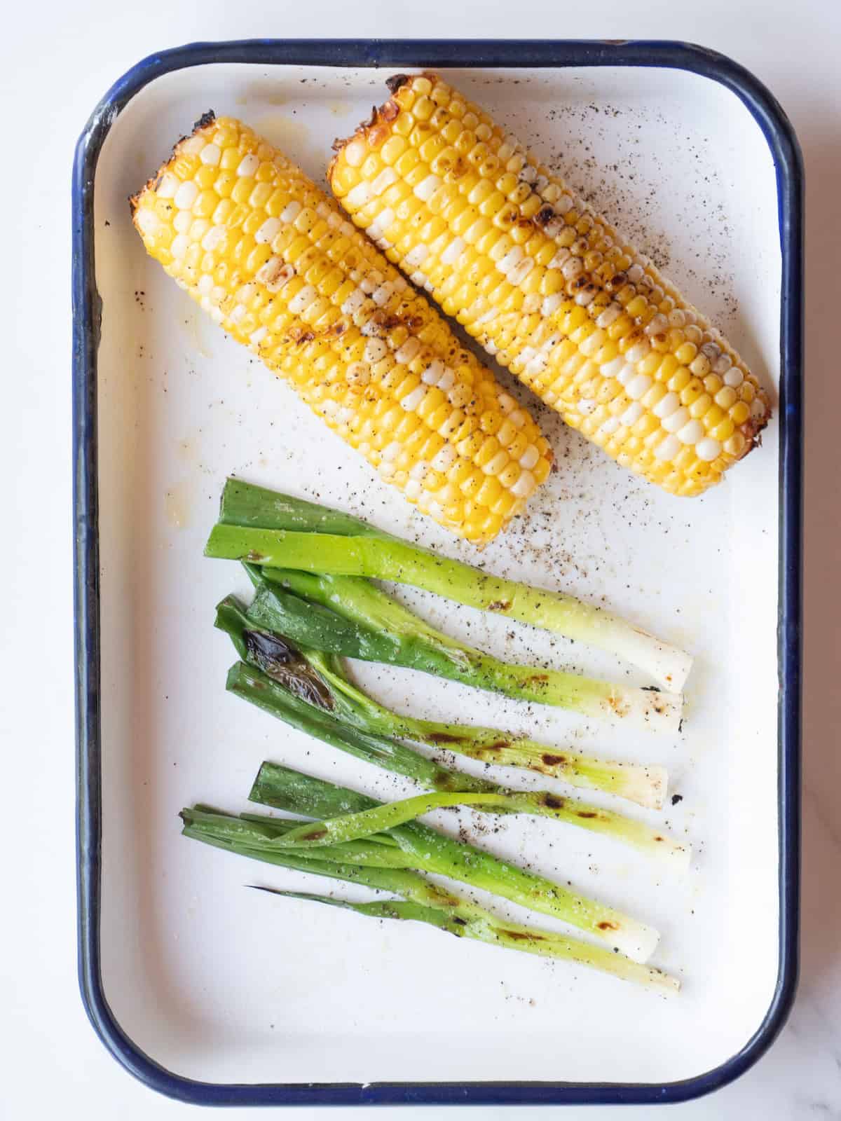 A rectangular platter with green onions and corn grilled with a slight char.