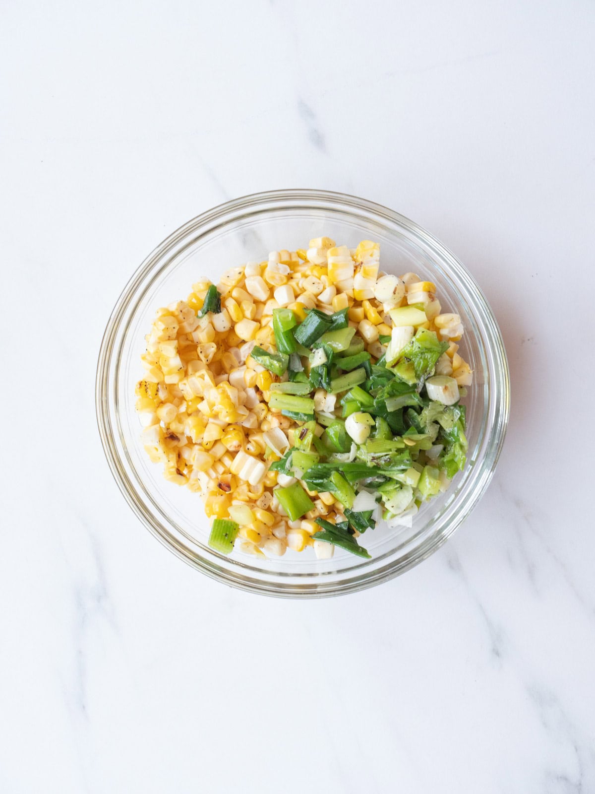 A mixing bowl with corn kernels and chopped green onions.