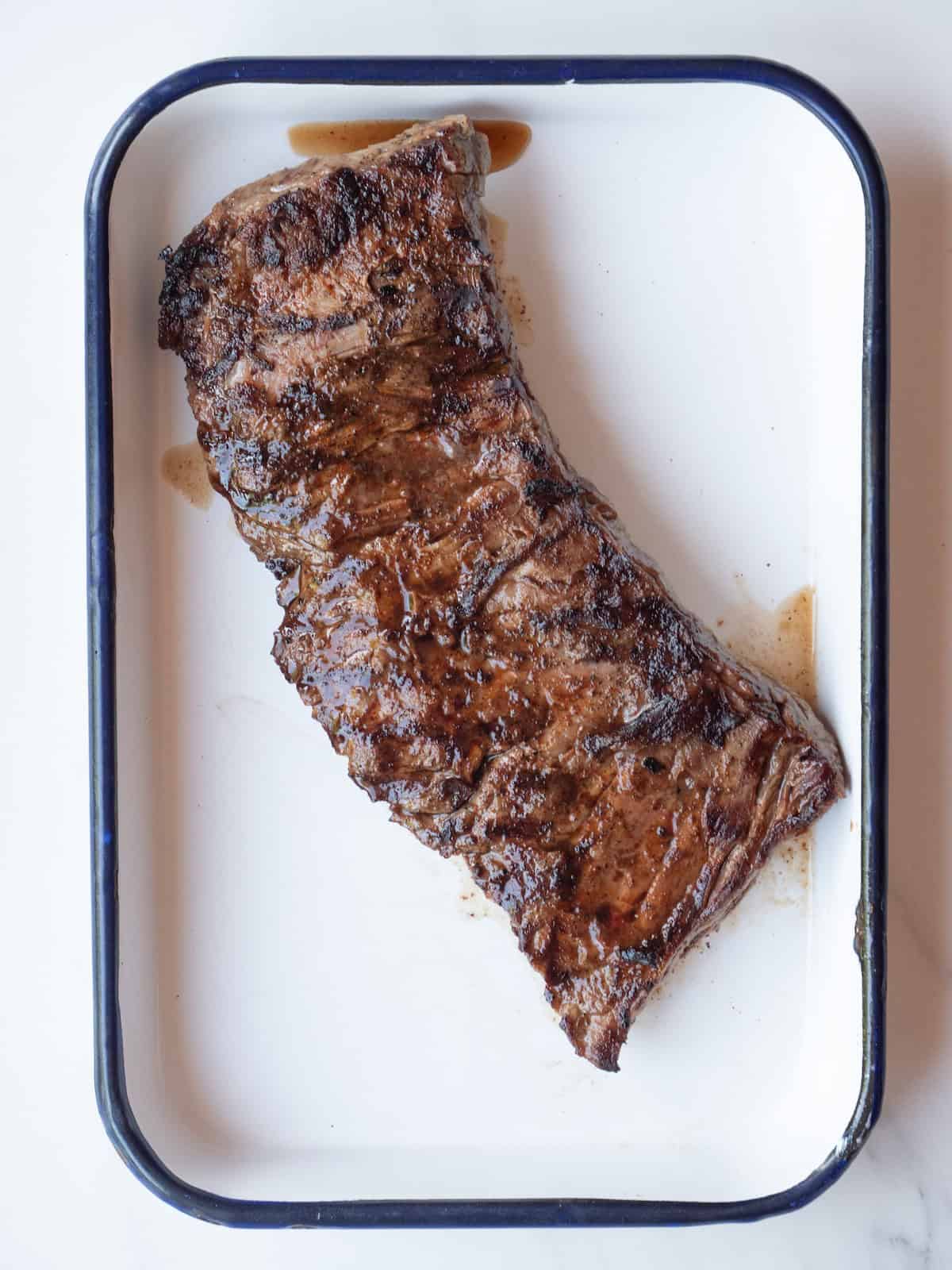 A rectangular platter with skirt steak grilled on both sides, and being rested.