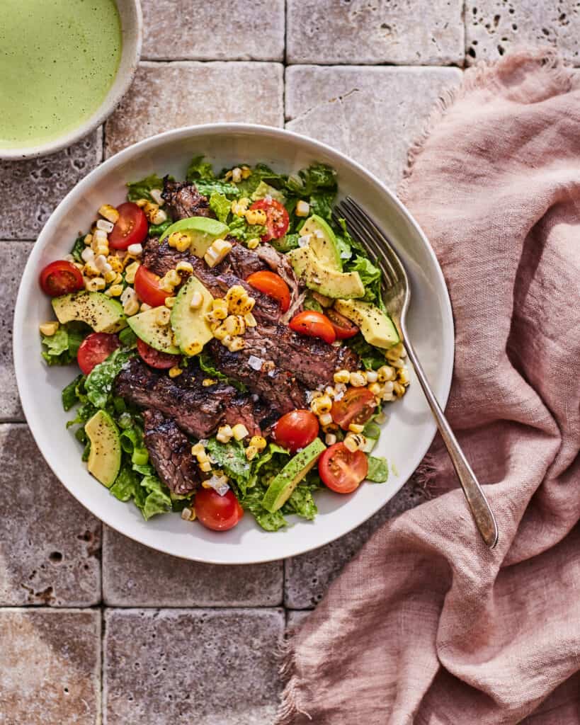 A bowl with a steak salad with a yogurt green goddess dressing on the side in a bowl.