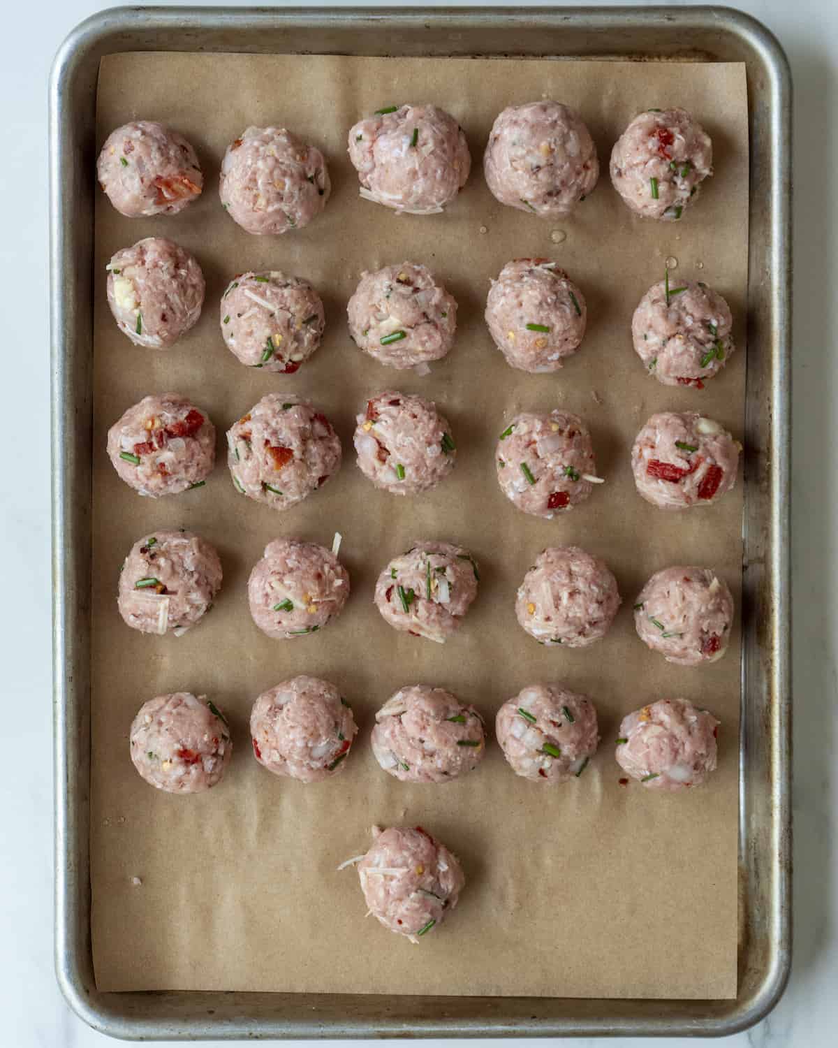 A parchment paper-lined sheet pan with raw turkey meatballs.