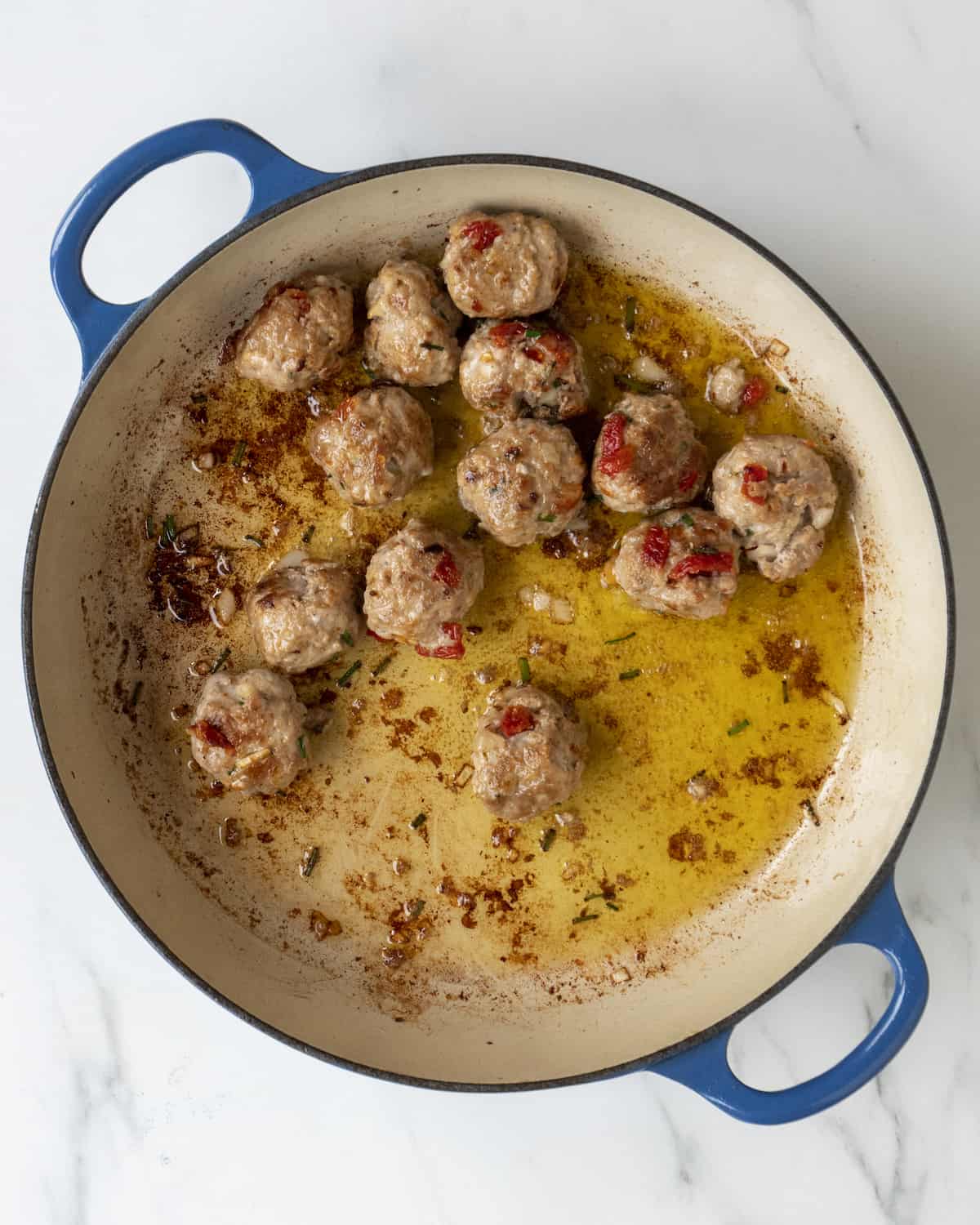 A blue dutch oven with turkey meatballs being cooked in olive oil.