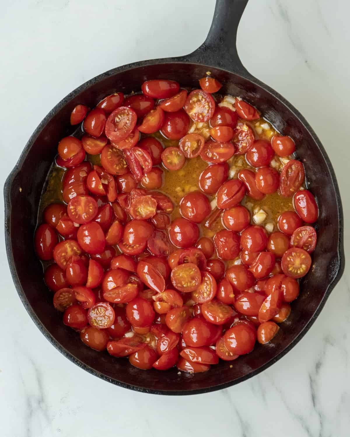A skillet with cherry tomatoes being cooked in oil and garlic.