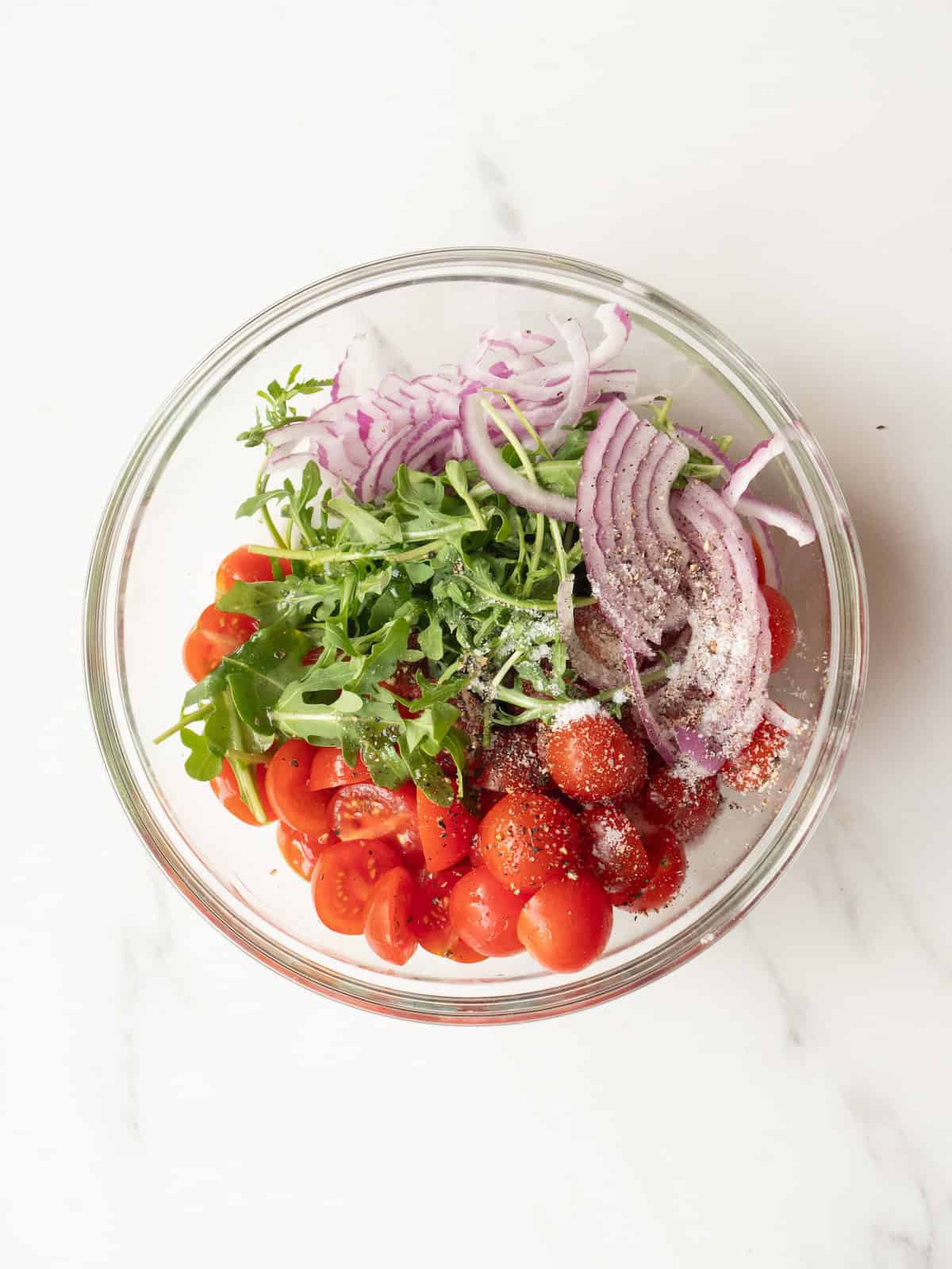 A mixing bowl with a cherry tomato salad made with arugula and red onions.